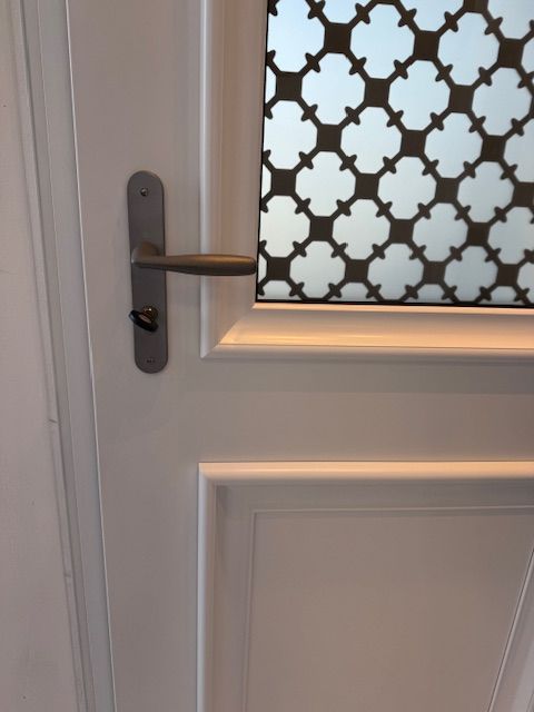 Gros plan sur une porte blanche avec une poignée en laiton et un panneau décoratif en verre dépoli.