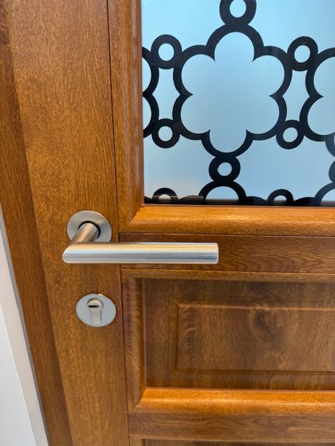 Porte en bois avec poignée et serrure argentées, laissant apparaître du verre dépoli à motif décoratif noir.