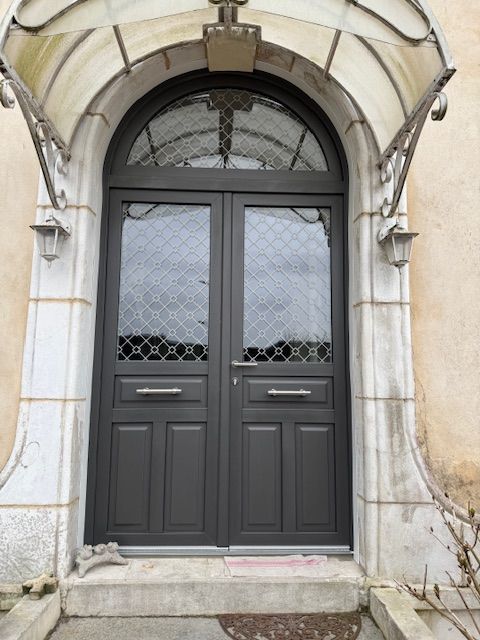 Double porte d'entrée sombre sous une arche en pierre avec une petite marche et des détails en fer forgé