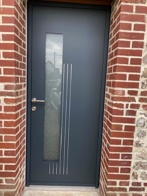 Porte d'entrée gris foncé avec un étroit panneau de verre dépoli dans un encadrement de porte en briques rouges