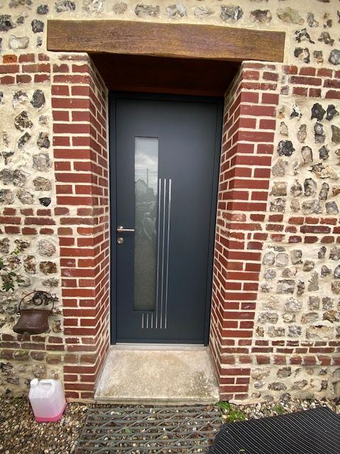 Porte d'entrée avec panneau bleu foncé, cadre en briques et en pierres, et un petit récipient rose sur la marche.