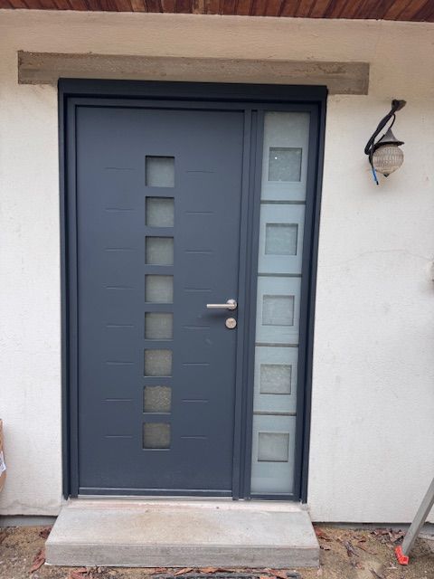 Porte d'entrée grise moderne avec panneaux de verre étroits et une applique murale à côté.
