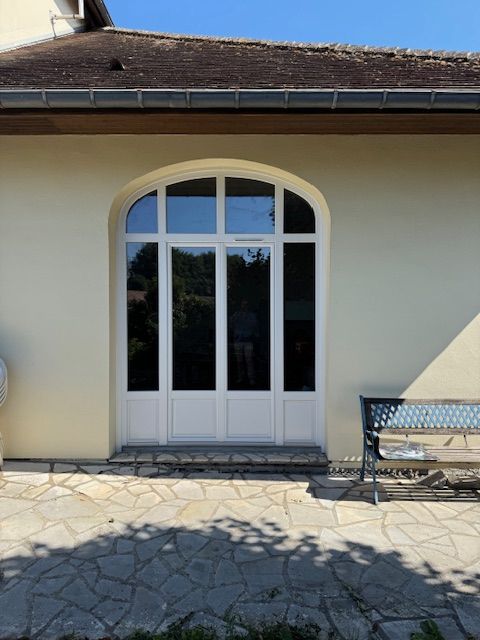 Porte vitrée cintrée blanche sur un mur en stuc, à côté d'une terrasse en pierre et d'un banc en métal.