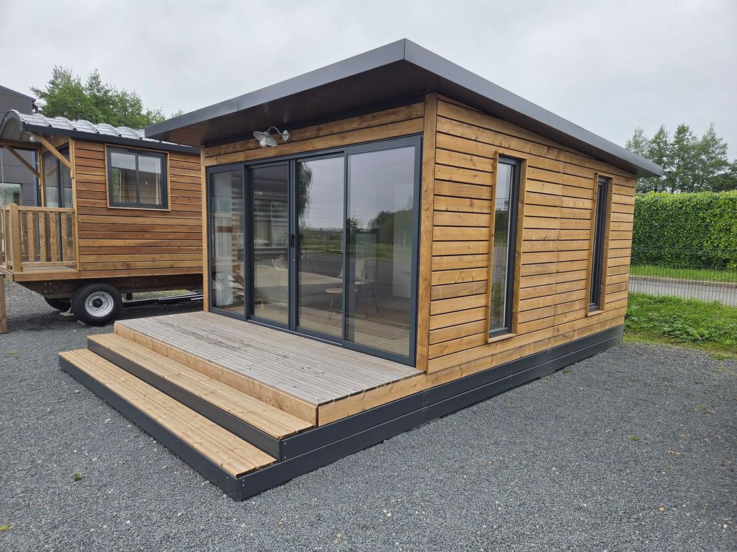 Petite cabane moderne en bois avec de grandes portes vitrées et une petite véranda sur un terrain gravillonné