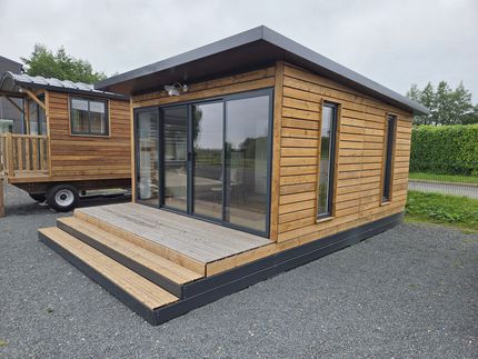 Petite cabane moderne en bois avec de grandes portes vitrées et une petite véranda sur un terrain gravillonné