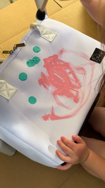Young child painting a Mom’s Favorite white insulated tote bag by The Stever Co. with colorful handprint-style artwork for a personalized keepsake gift.