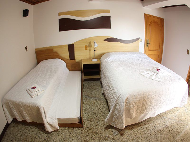 Um quarto de hotel com duas camas cobertas de branco, uma pequena mesa de cabeceira entre elas e decoração de parede em tons de bege e marrom.