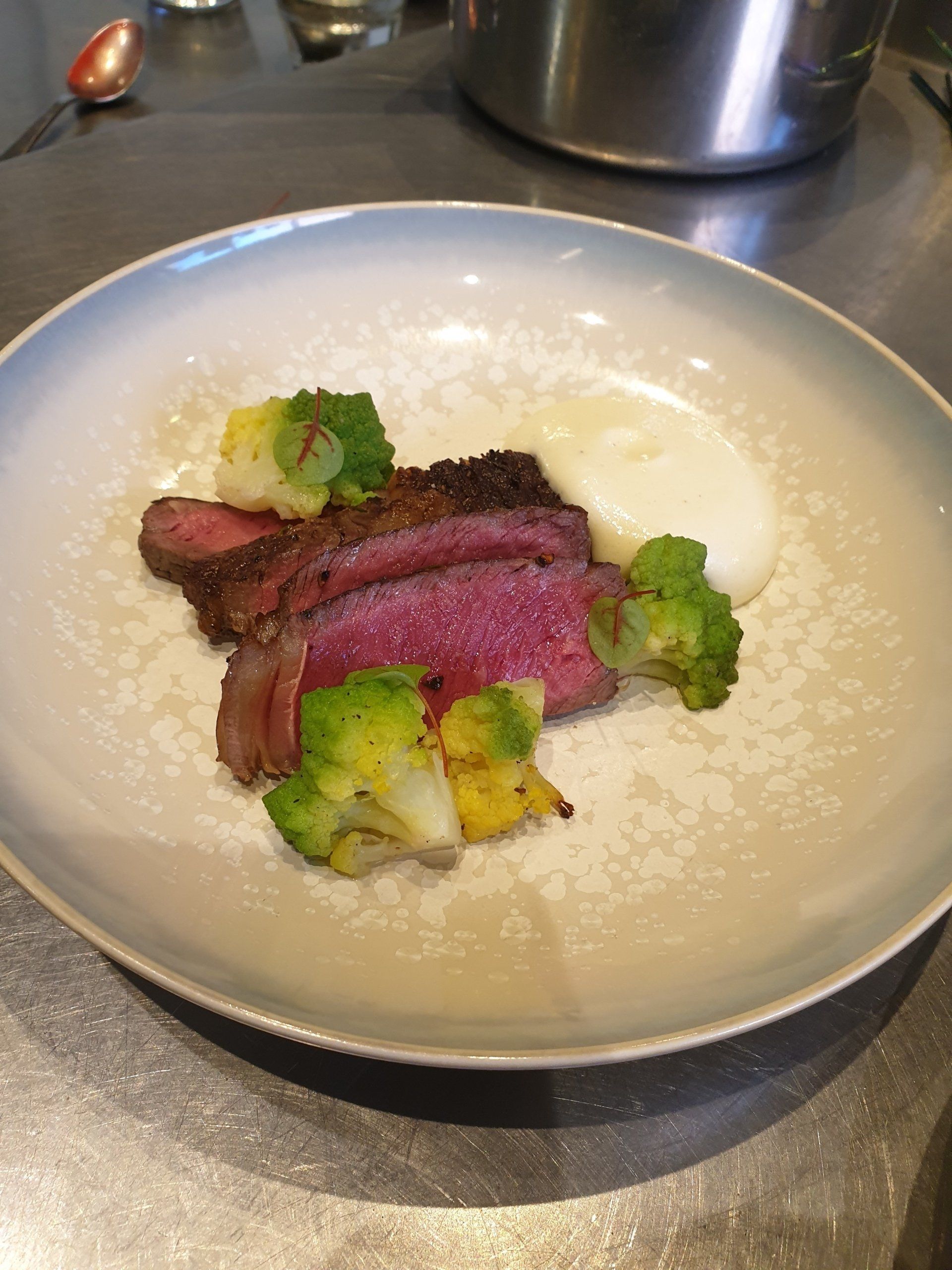 Sliced steak with roasted broccoli and a dollop of white purée on a white plate.