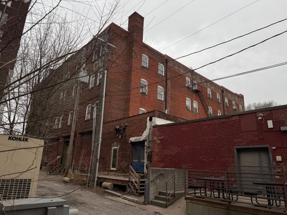 Brick industrial building with multiple stories, windows, and a chimney on a cloudy day.