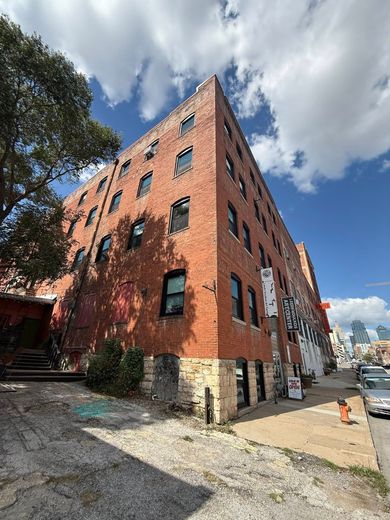 Brick building with arched windows under a blue sky. City sidewalk and street.