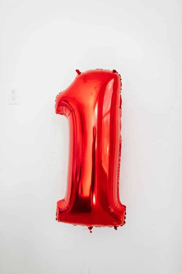 Red foil balloon in the shape of the number one, hanging on a white wall.
