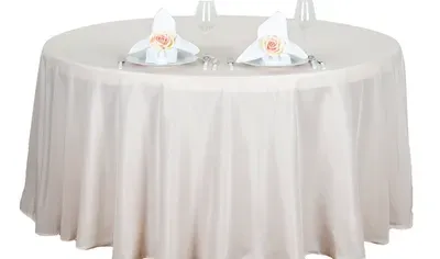 Round table with beige tablecloth, set with plates, napkins, and glasses.