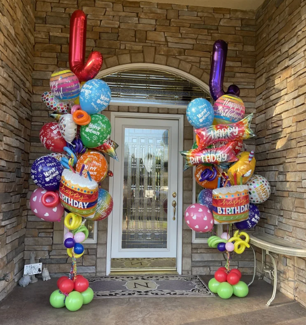 Birthday balloon columns flank a front door. Red, green, blue, and pink balloons make up the decorations.