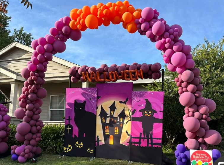 Halloween arch with purple, orange balloons, backdrop with black cat, haunted house, scarecrow.