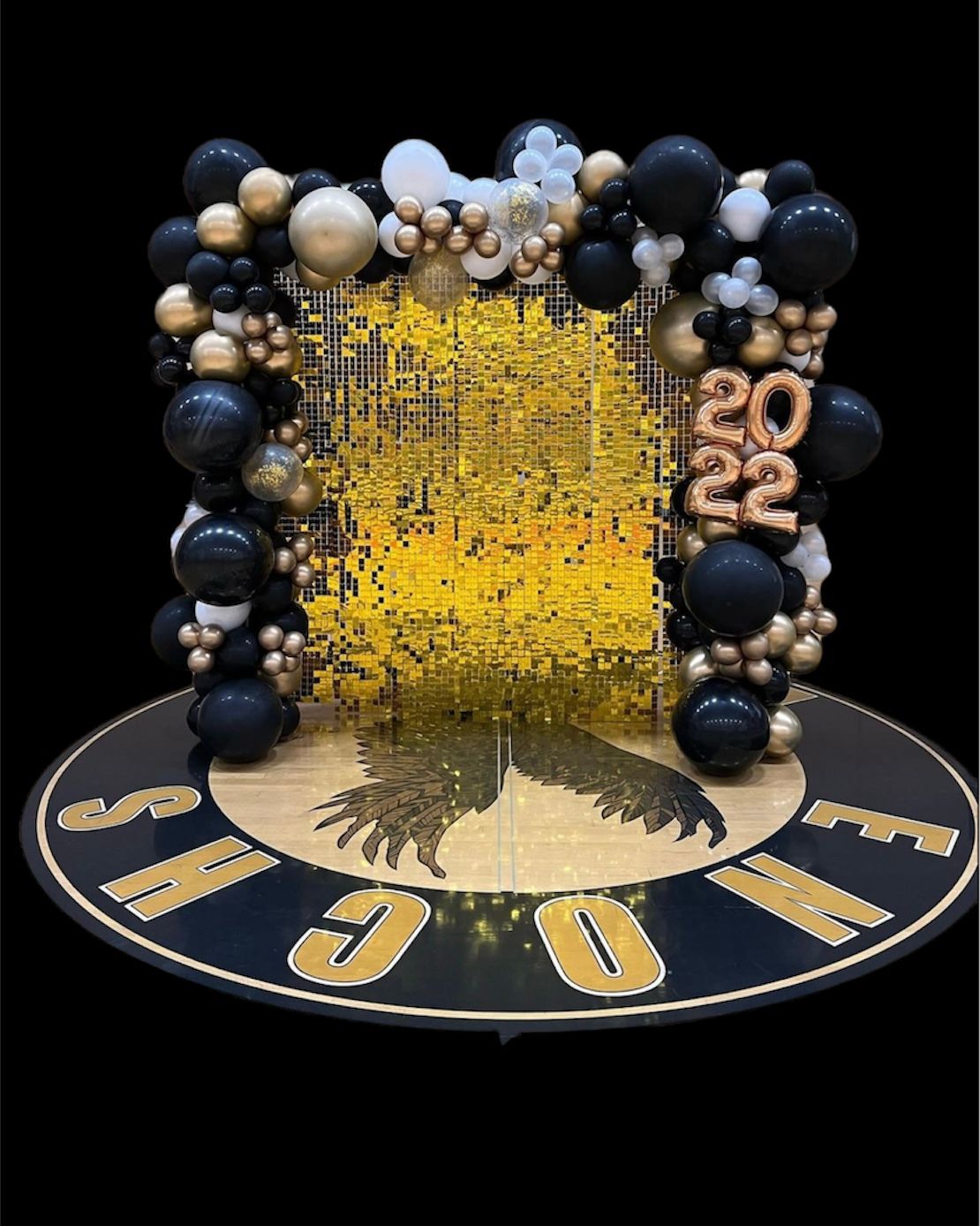 Black and gold graduation photo backdrop with balloons and 2022 numerals, on a floor with