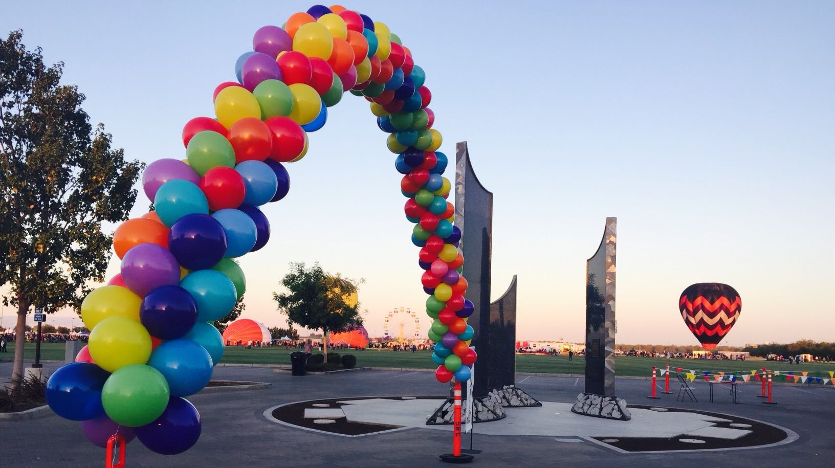 Rainbow balloon arch over memorial, hot air balloon rising in sky at dusk.