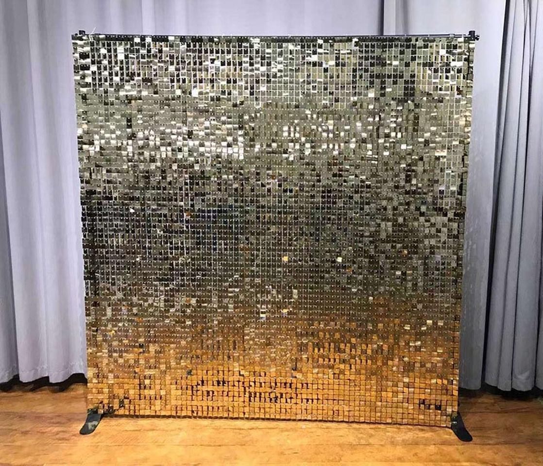 Gold sequin backdrop for a photo booth, standing on a wooden floor.