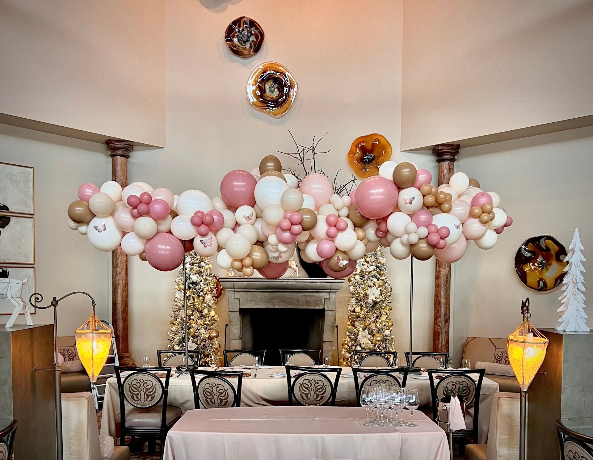 A festive dining table decorated with pink, white, and gold balloons, lights, and decor.