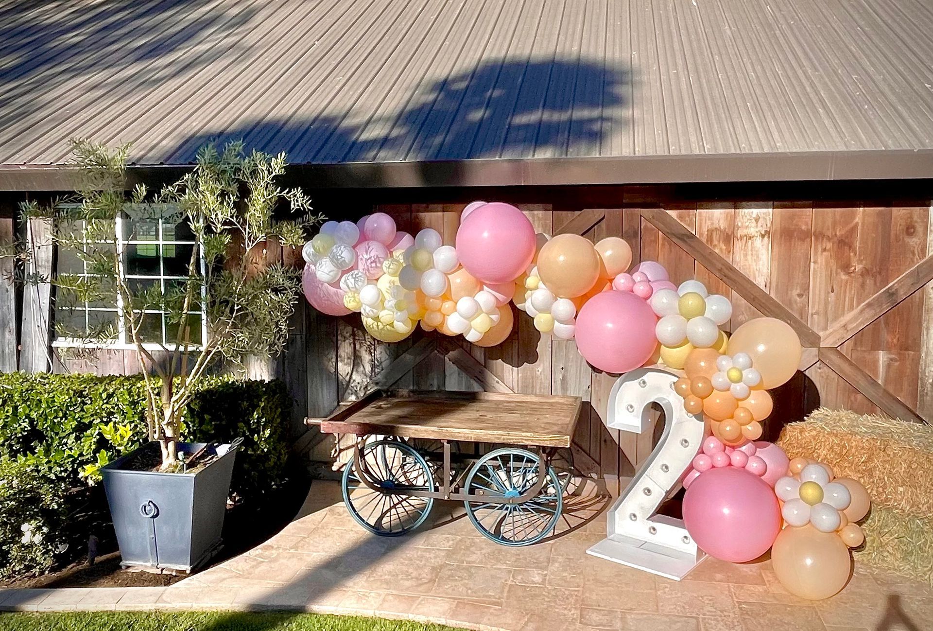 Birthday scene: Pink and peach balloon arch over a cart with a lit