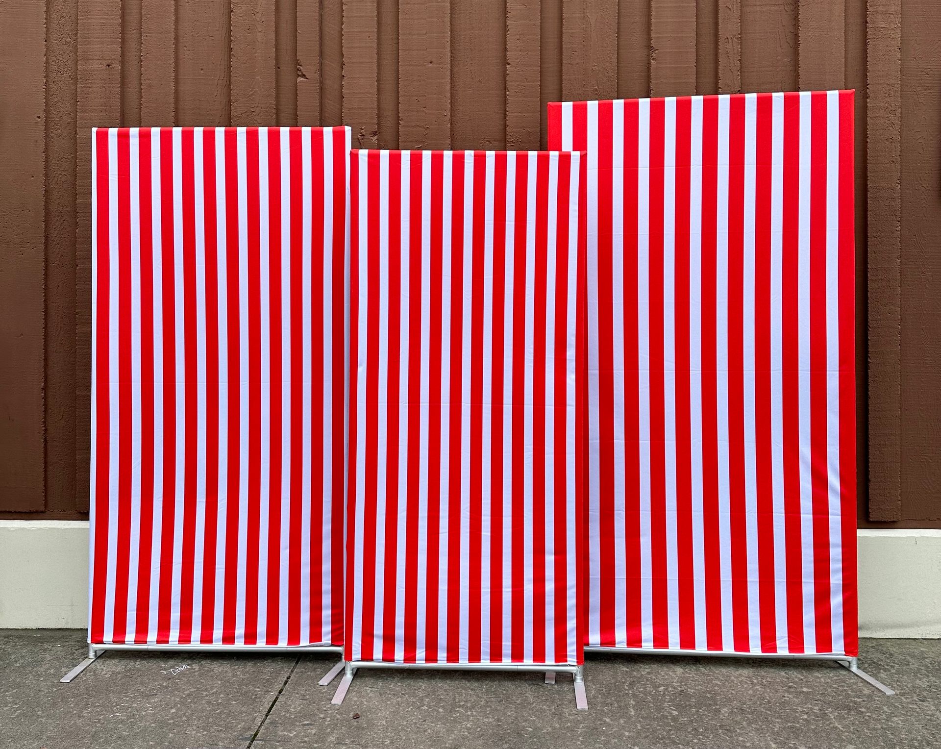 Three red and white striped panels of varying heights, propped against a brown wooden wall.