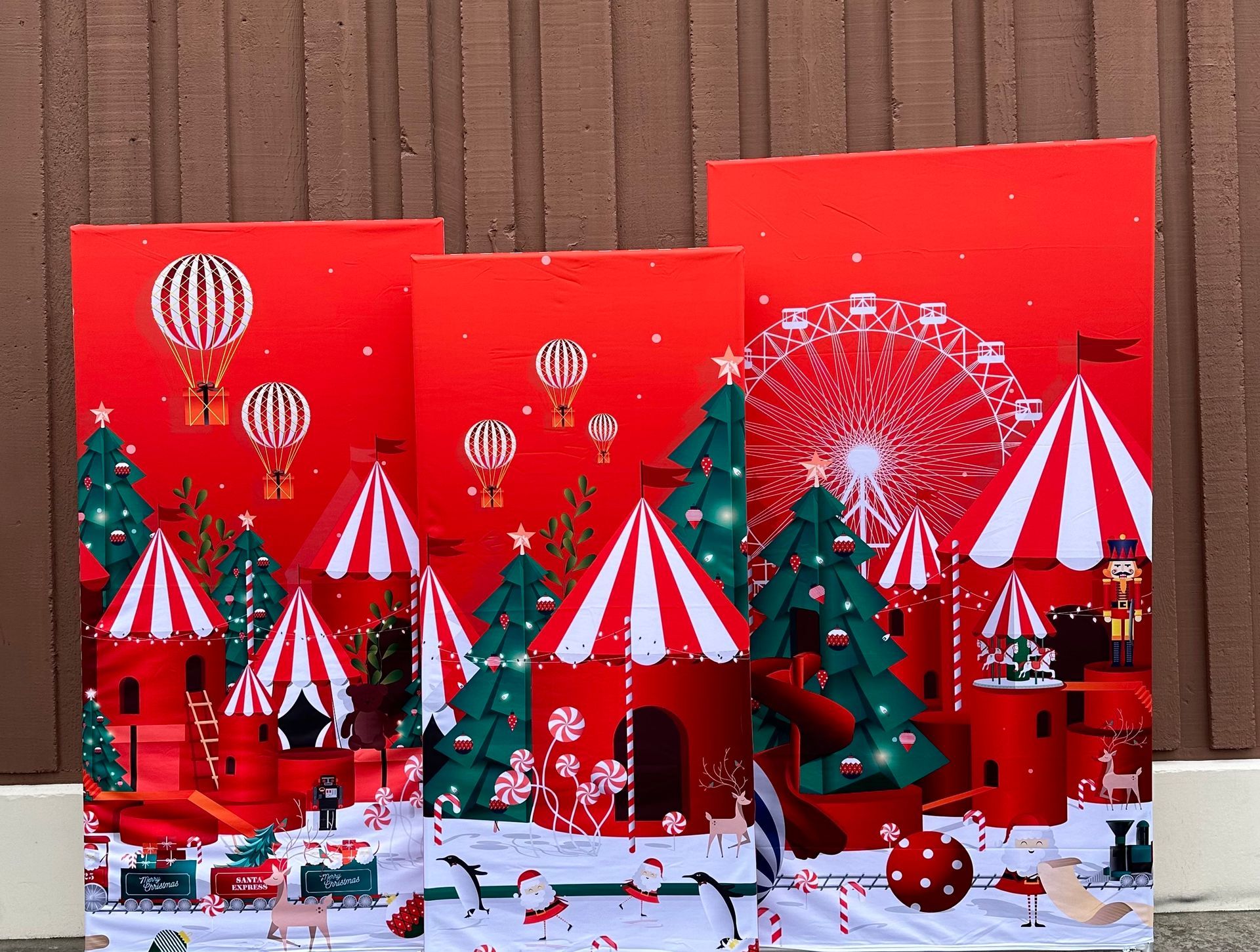Christmas-themed carnival display with tents, Ferris wheel, hot air balloons, and Santa on a red background.