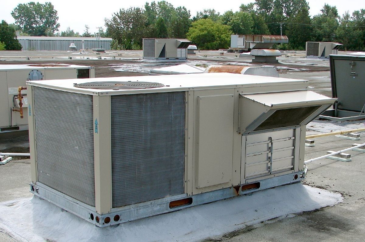 Large rooftop HVAC unit with metal vents on a flat commercial roof under a cloudy sky