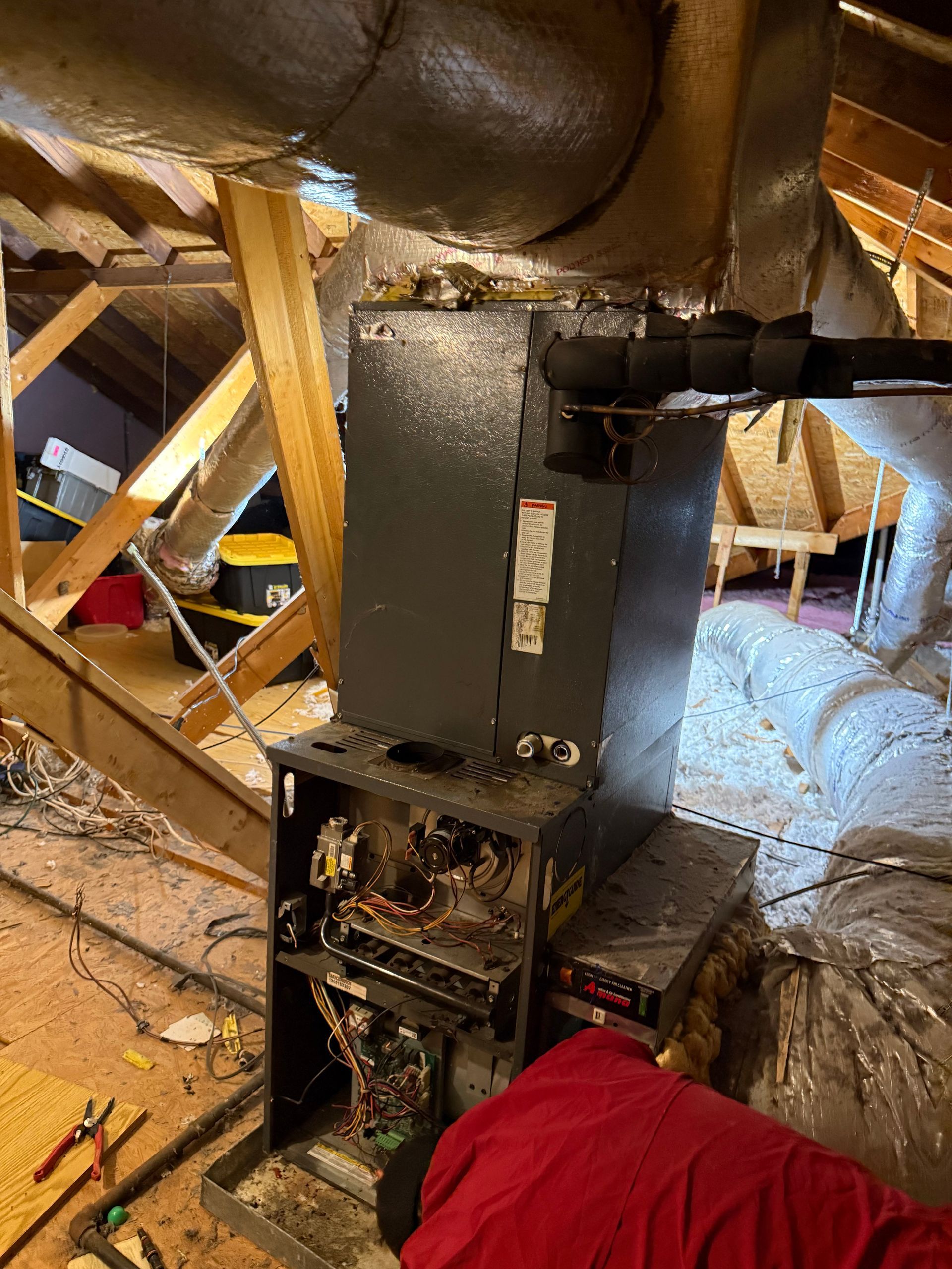 Black furnace in attic with exposed ducts, wooden beams, and a red cloth in the foreground