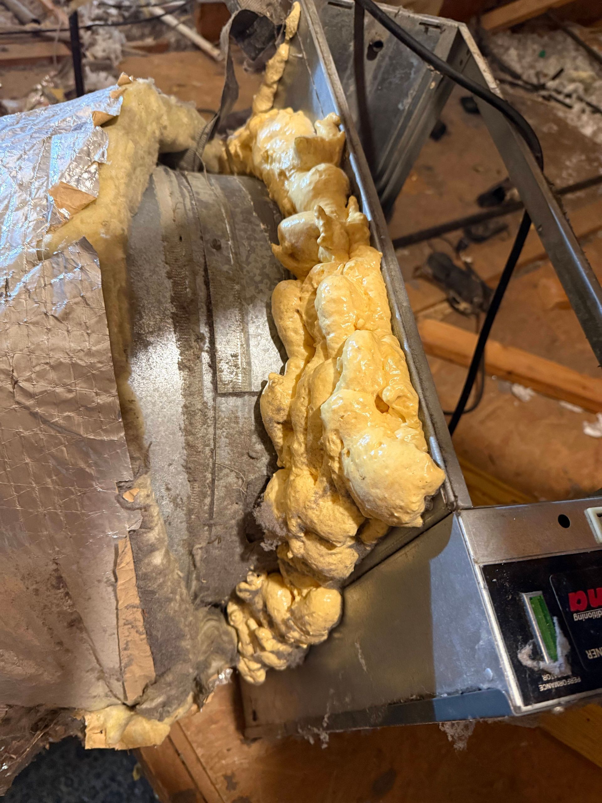 Foam-insulated ductwork and metal HVAC equipment inside an unfinished attic or crawl space