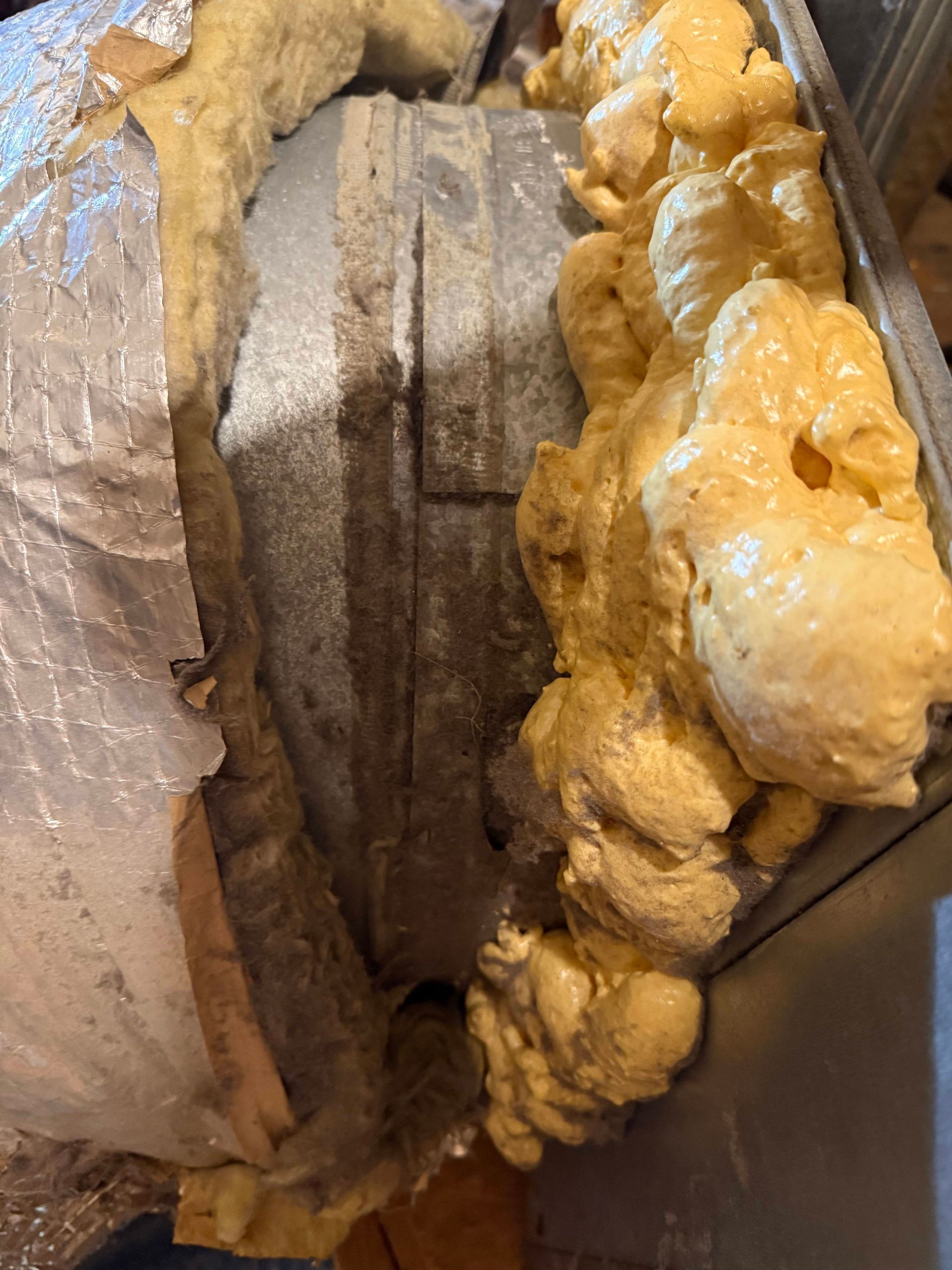 Close-up of a damaged wooden beam with expanding foam insulation filling gaps around it.