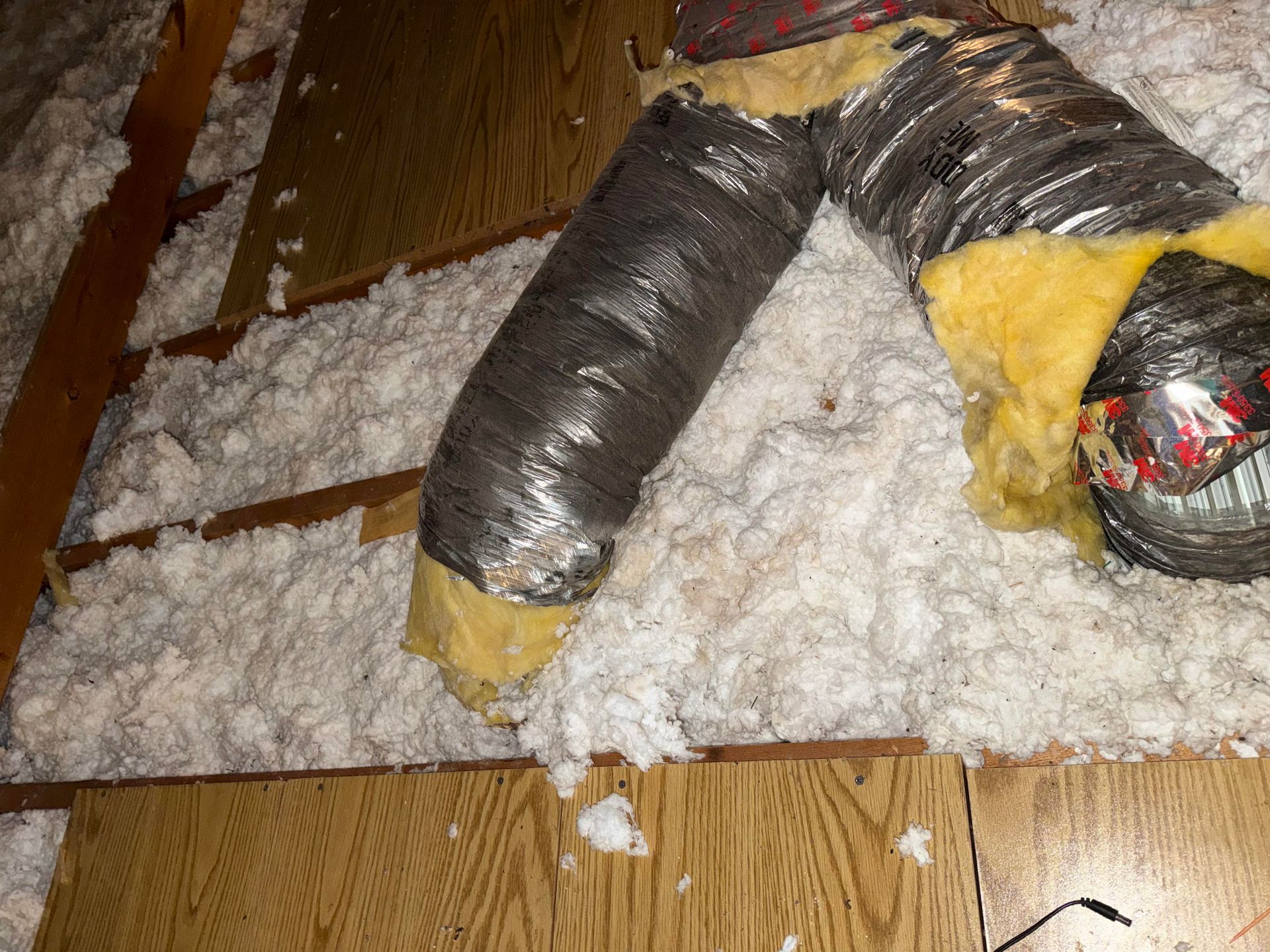Severely damaged air duct with torn black insulation and yellow lining on a snowy floor indoors