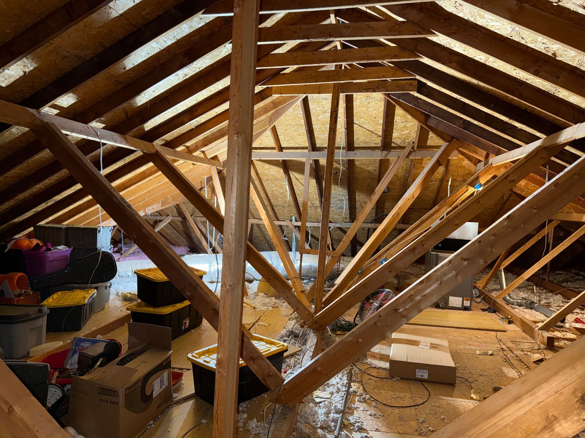 Attic under renovation with exposed wooden roof beams, scattered tools, and construction materials on the floor