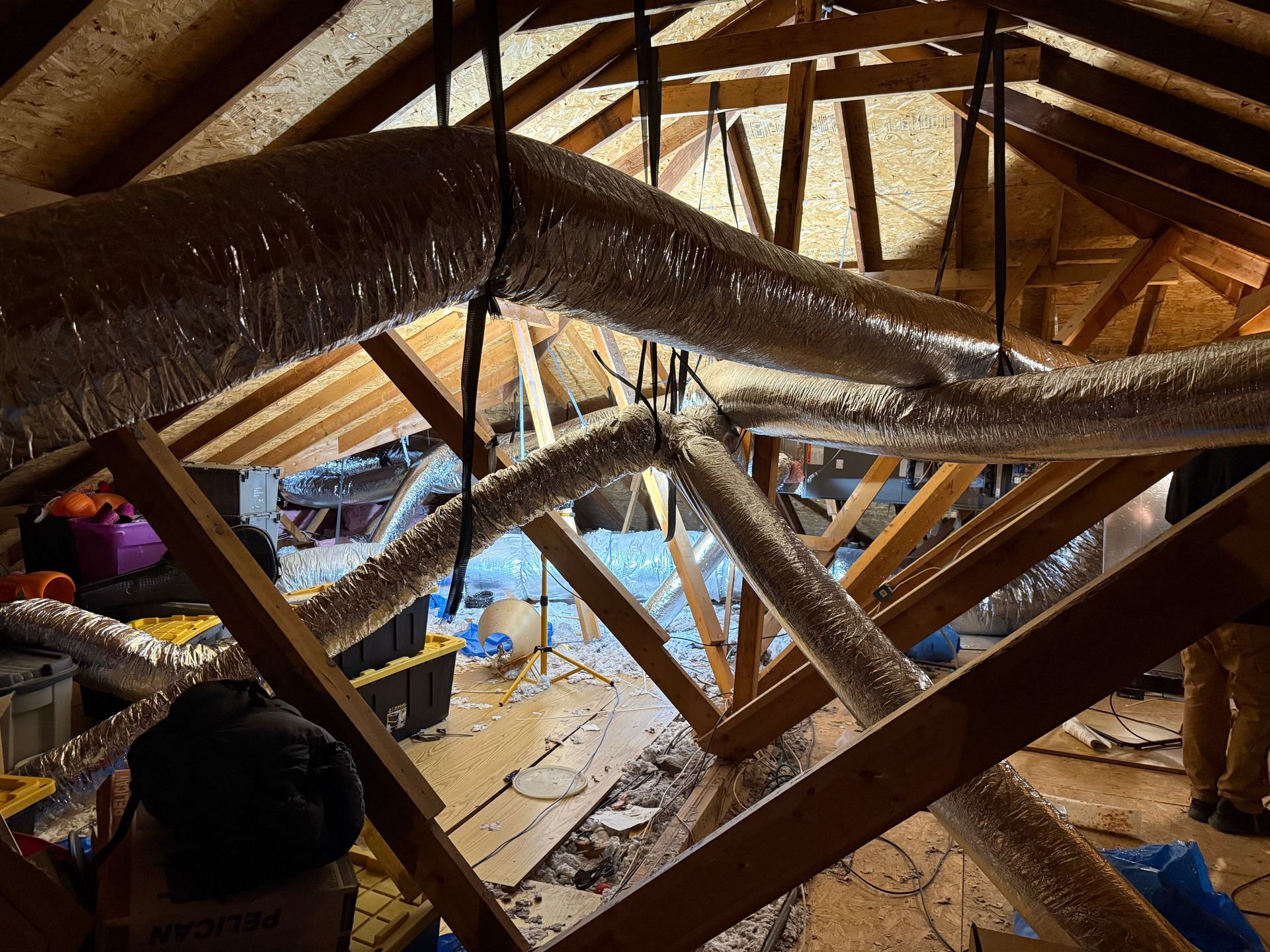 Attic framed with exposed ducts and beams; workers sort materials near a lit work area.
