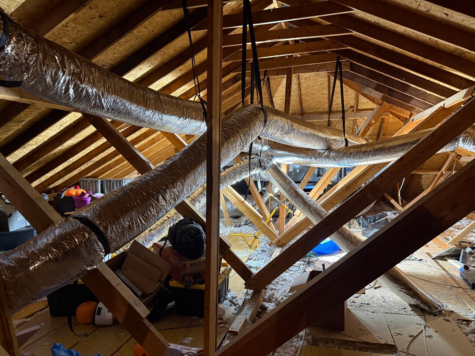 Attic with exposed wooden rafters and insulation, showing a person working amid beams and debris