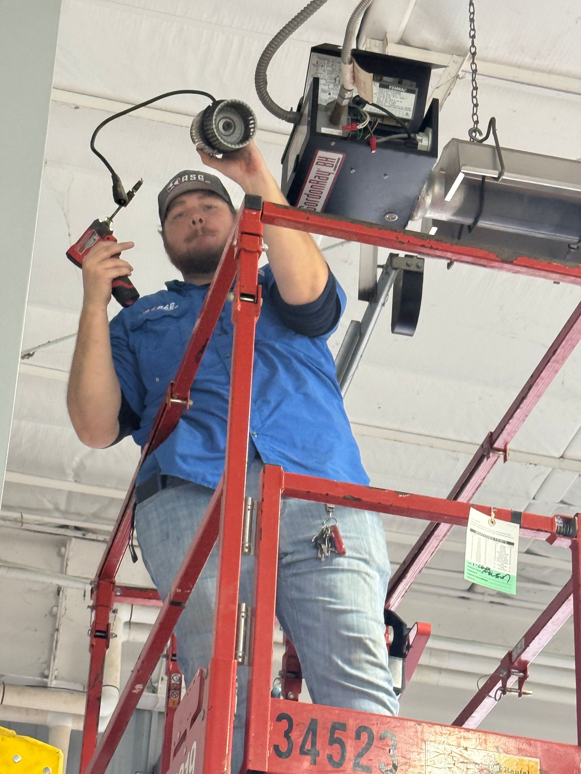 Worker in blue shirt and hard hat adjusting equipment from a red lift indoors