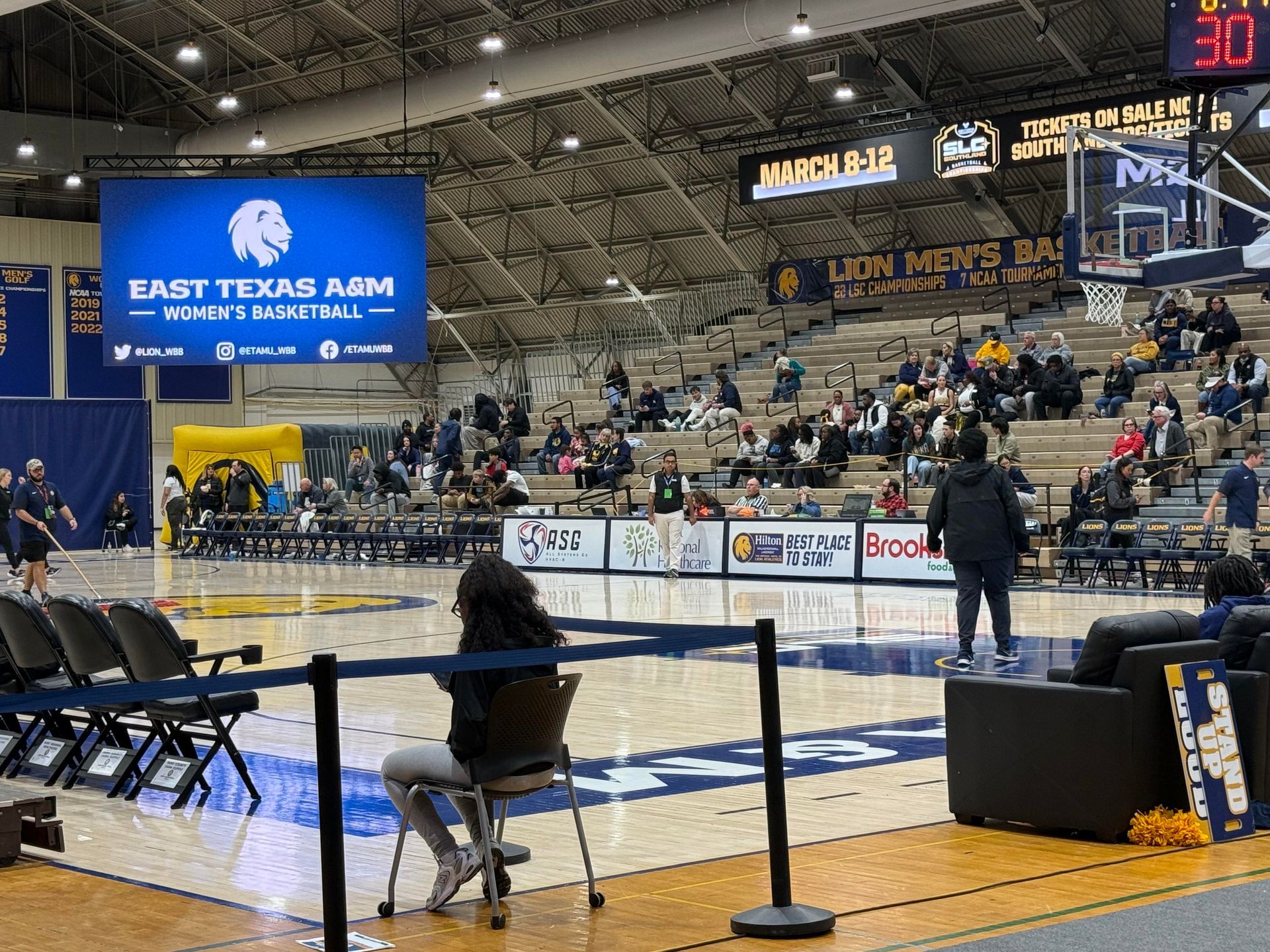 Indoor rodeo arena with a cowgirl on a horse and spectators in the stands, near a “Sart Tekas Arm” sign