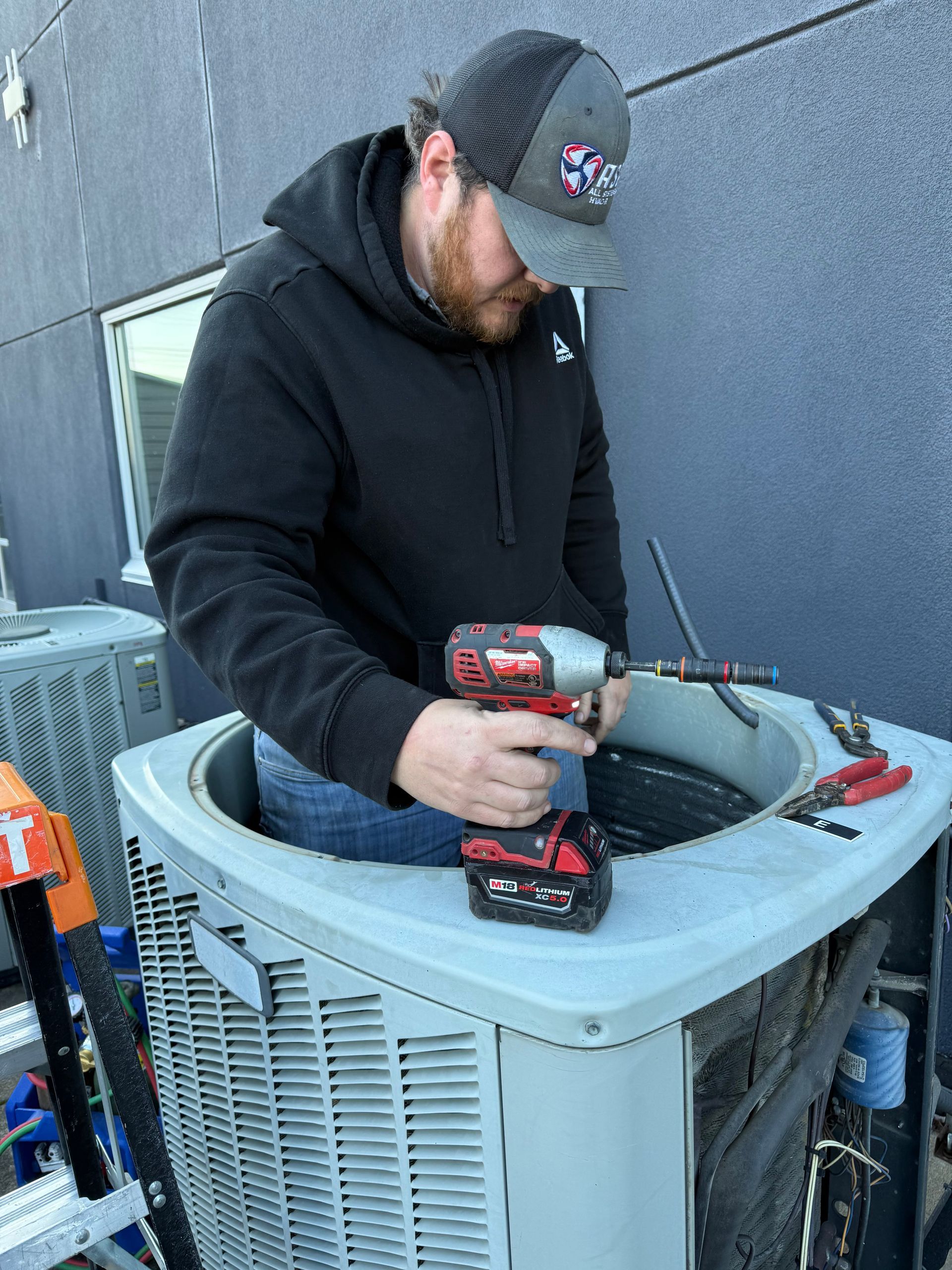 Technician using a red drill to repair a rooftop HVAC unit outdoors