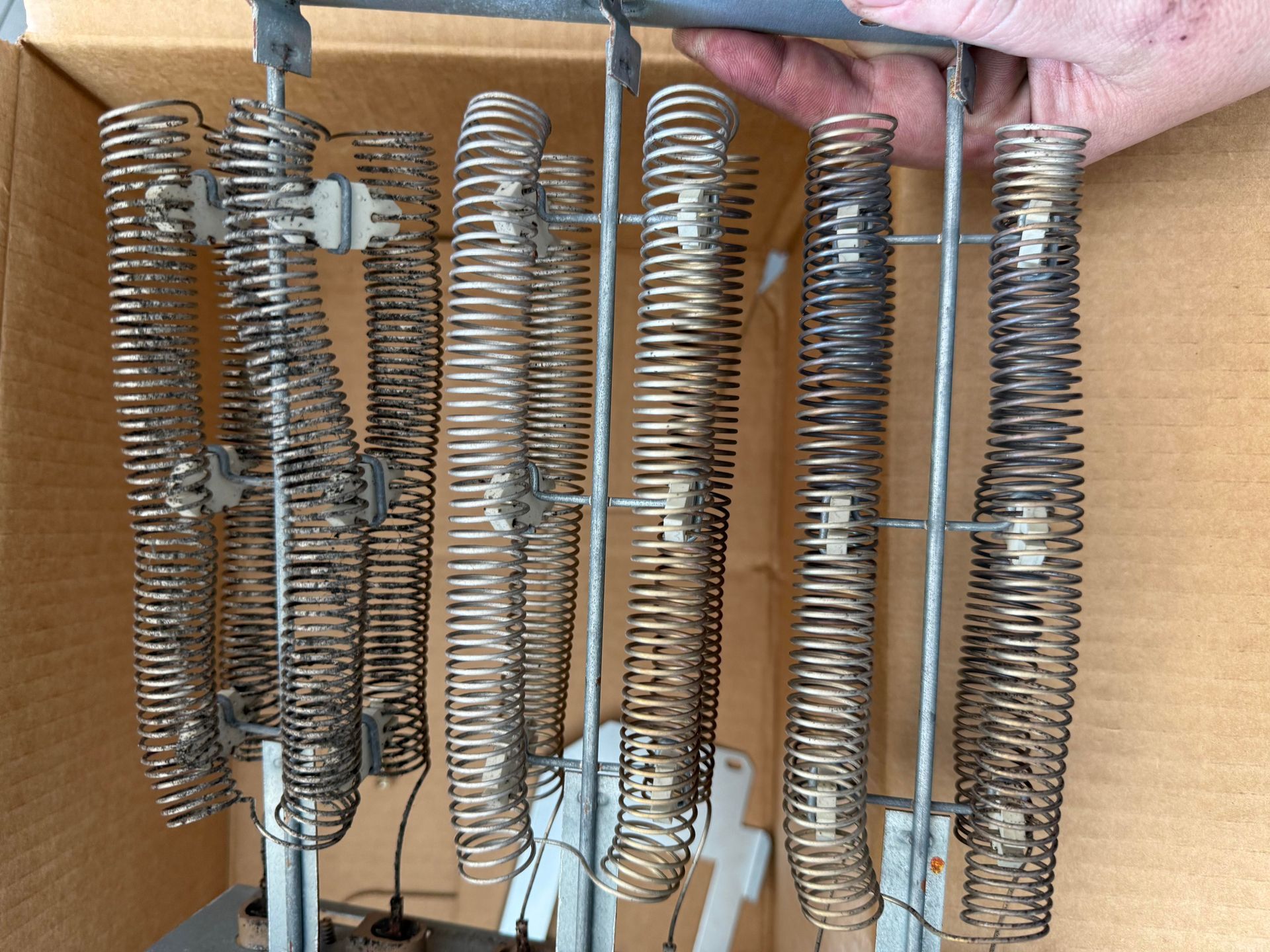 Metal spring coil assemblies with dark wire bases arranged in a cardboard box, held by a hand
