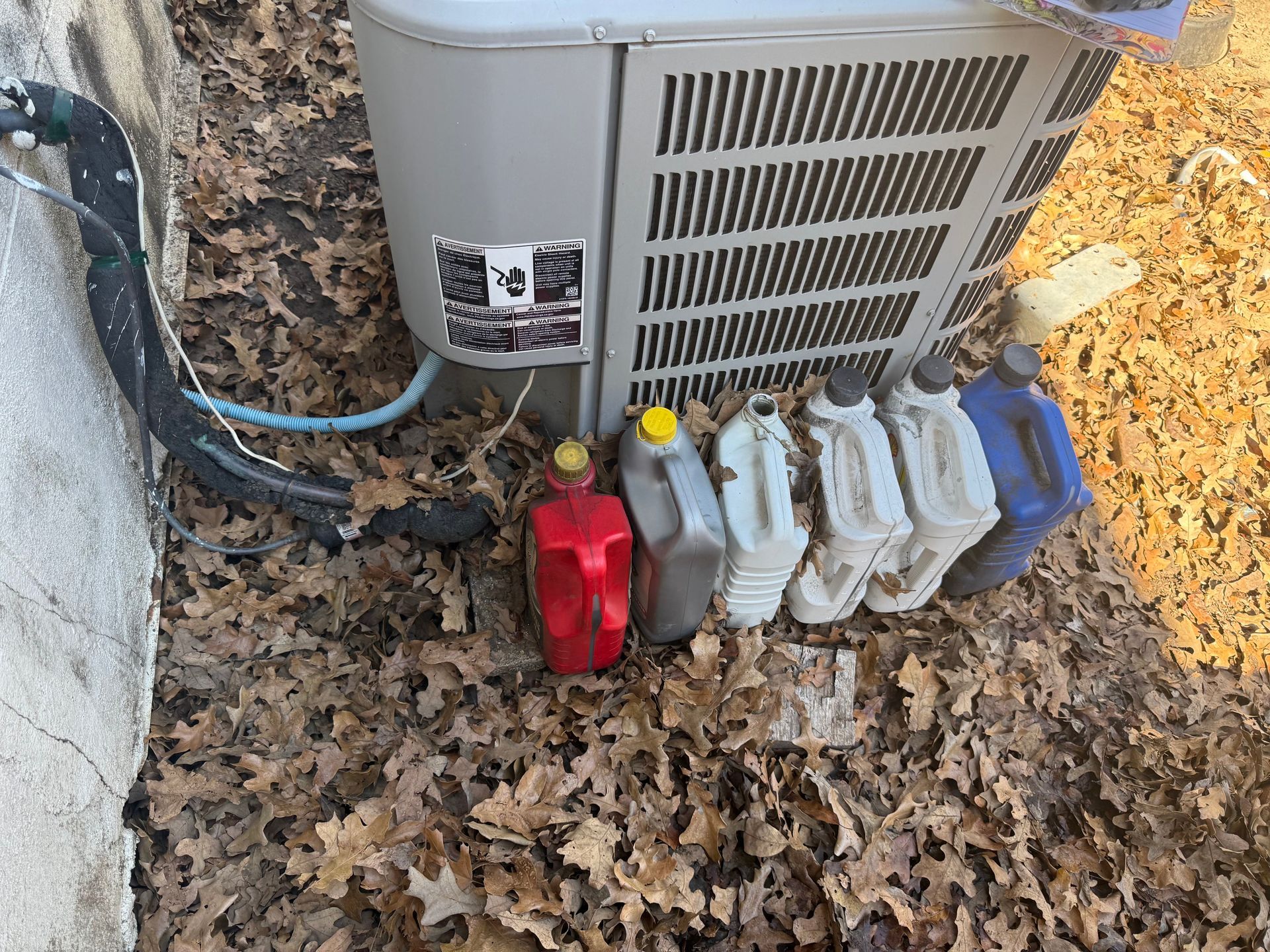 Outdoor HVAC unit with colorful refrigerant tanks and fallen leaves on the ground