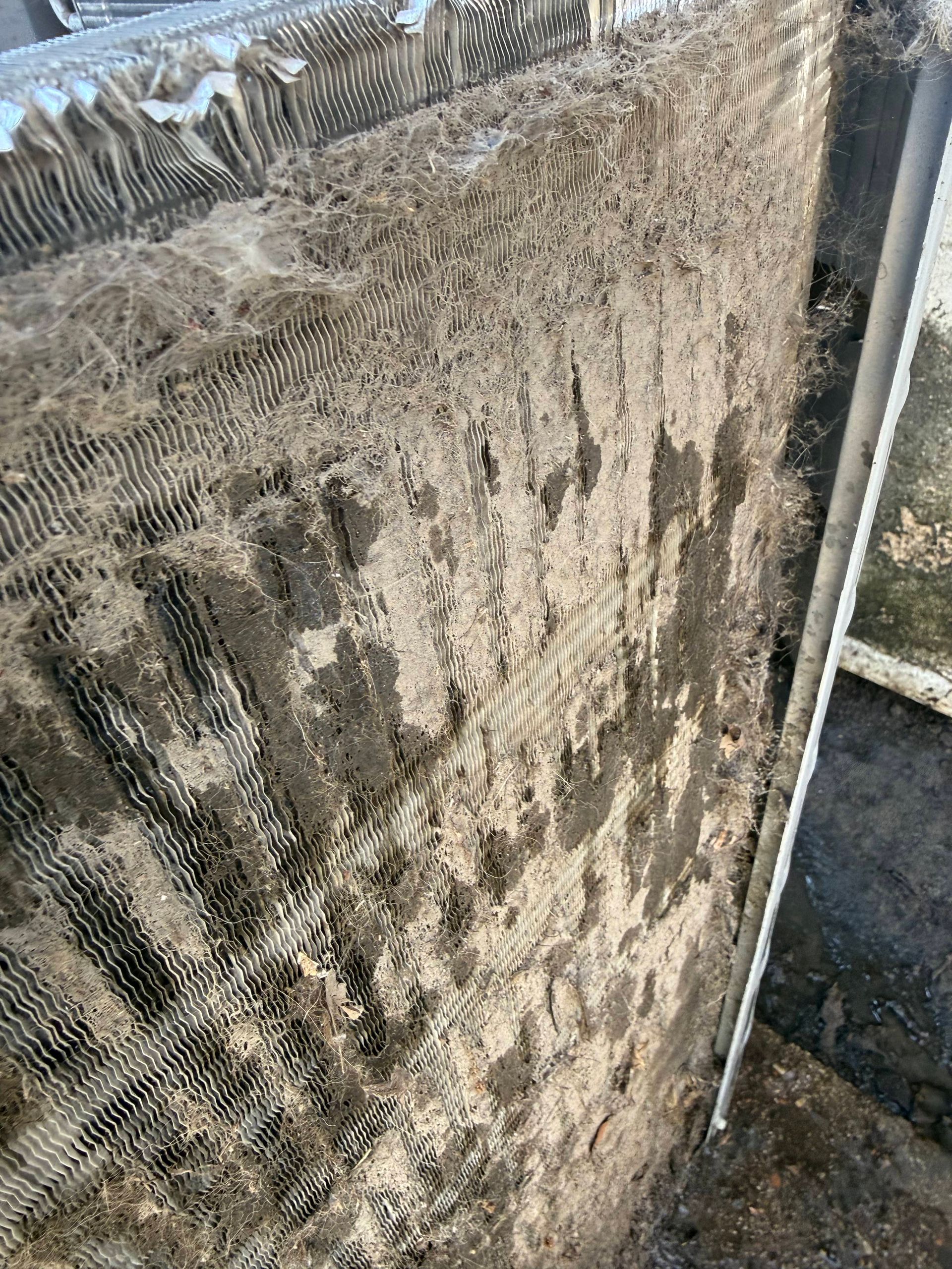 Dirty outdoor air-conditioning coil covered in dust and debris, with a heavily clogged surface.