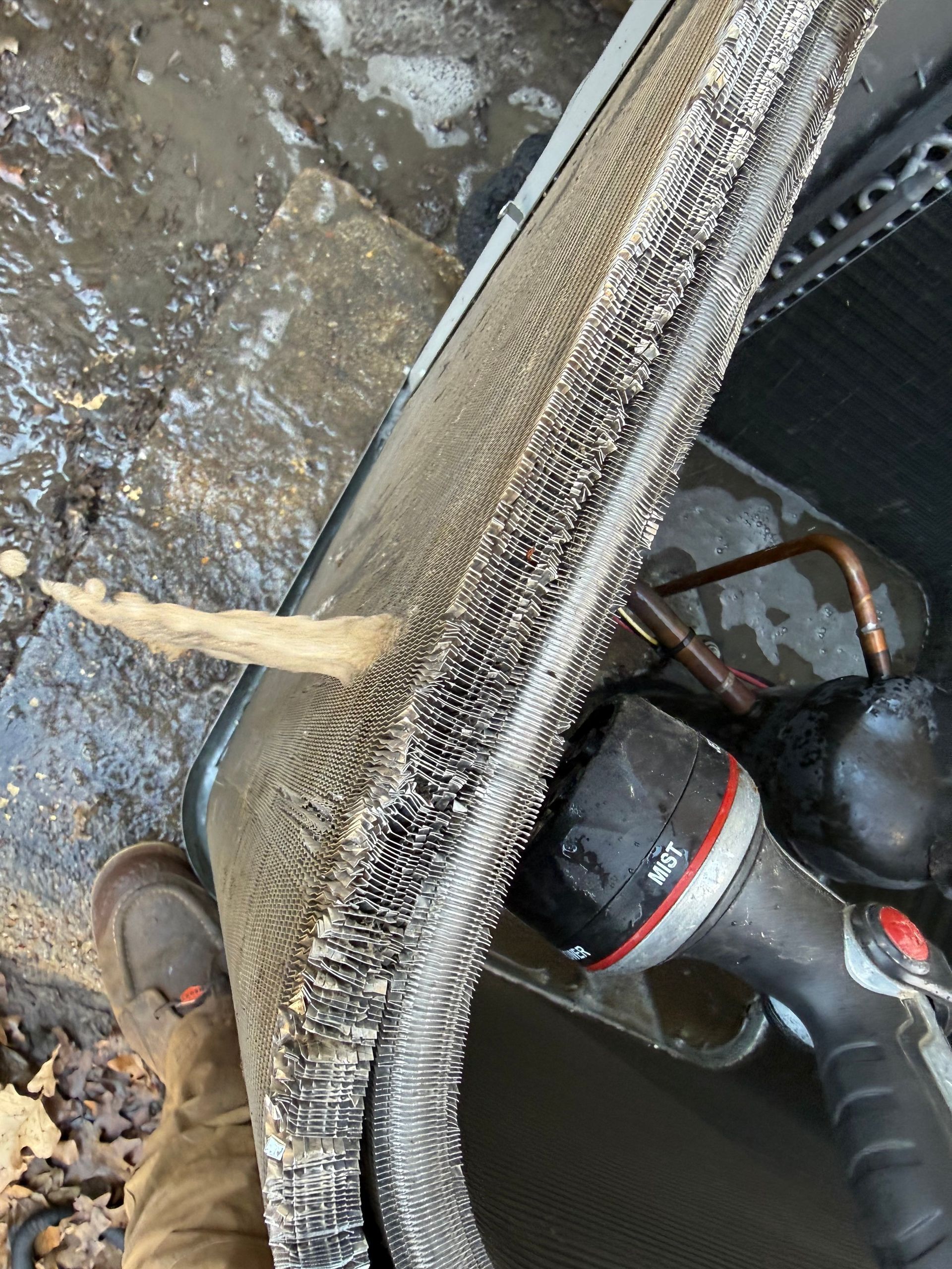 Close-up of a wet floor mat being lifted, with a vacuum cleaner and muddy ground visible.