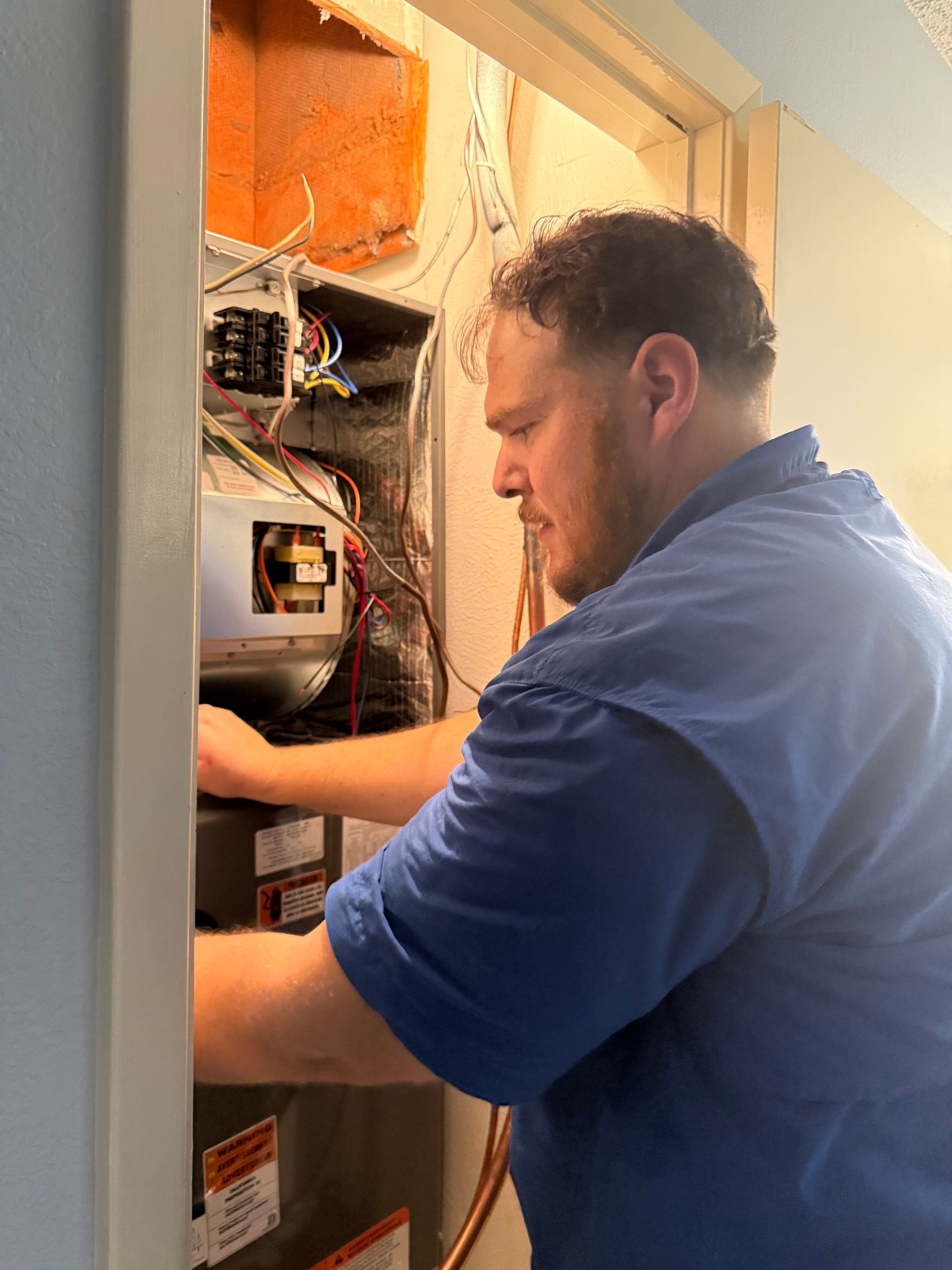 Technician working inside an open electrical panel in a wall, wearing a blue shirt.