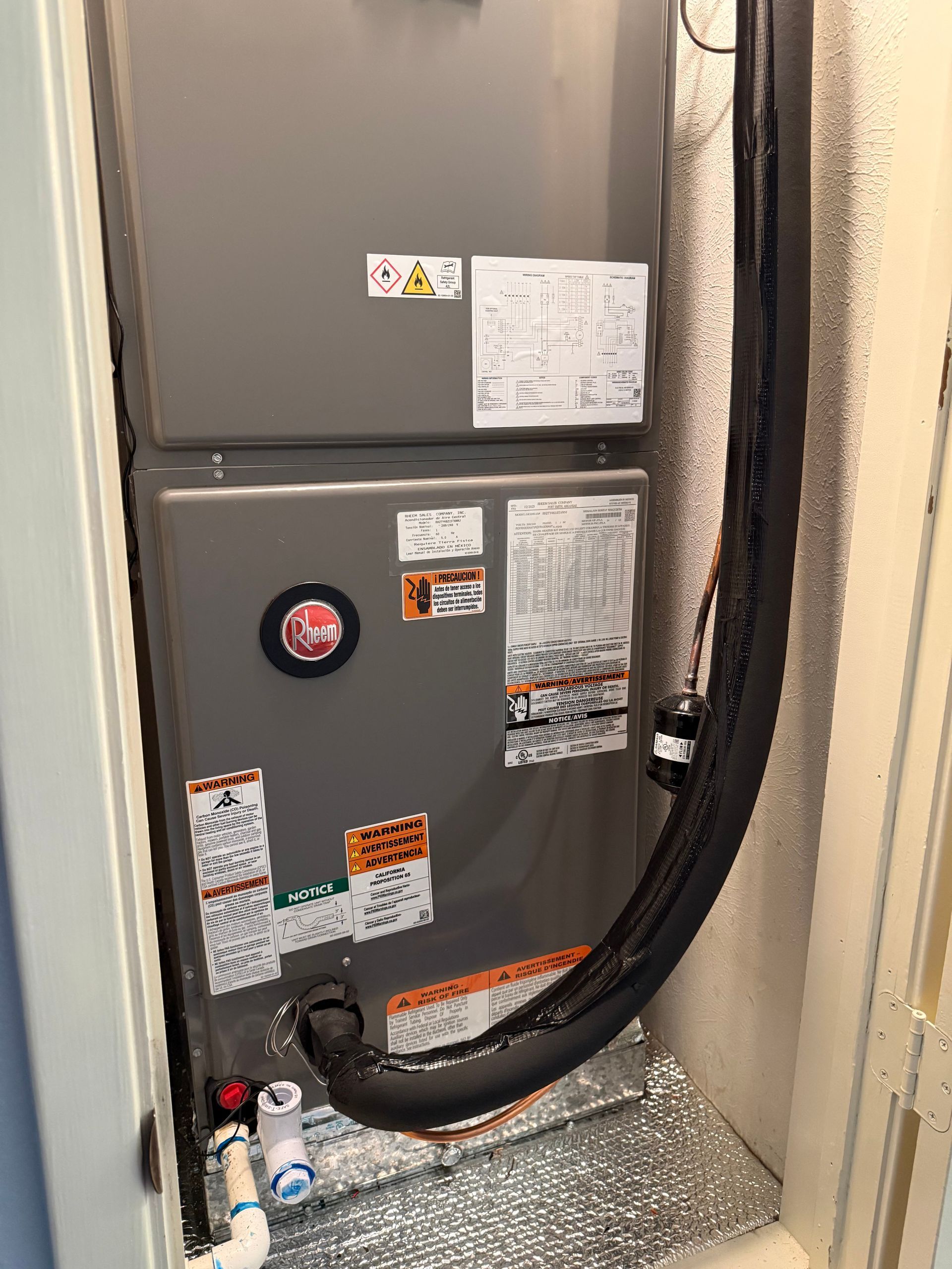 Gray HVAC unit with labels and insulated black hose in a utility closet