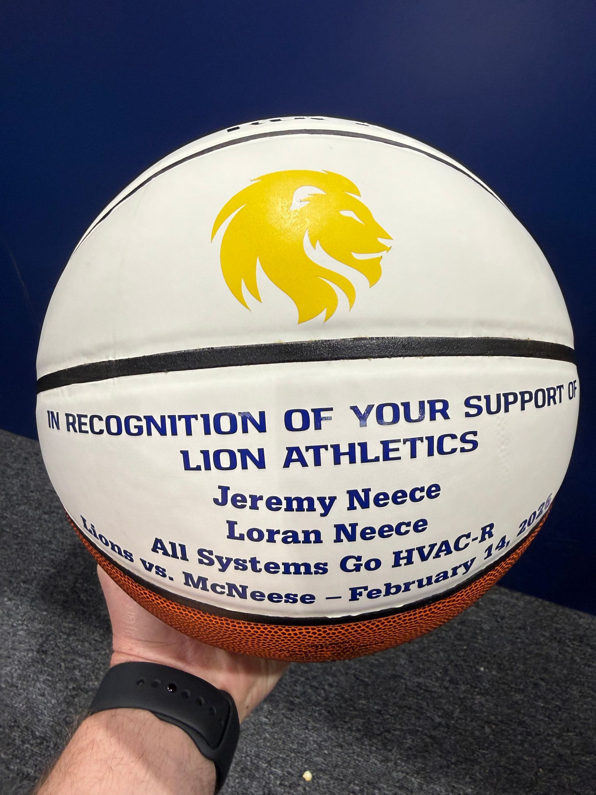 Signed white basketball with yellow lion logo and blue text held in a hand