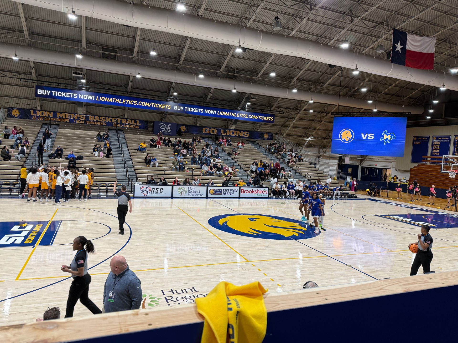 Indoor basketball game in a gym, with players on court and spectators in the stands.