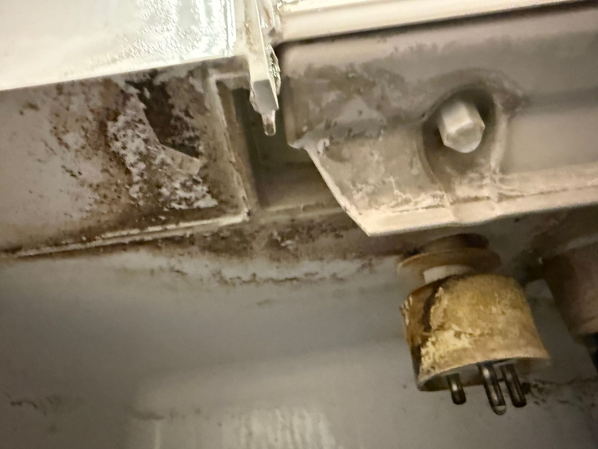 Close-up of a corroded metal underside with a leaking drip and a small electrical connector.