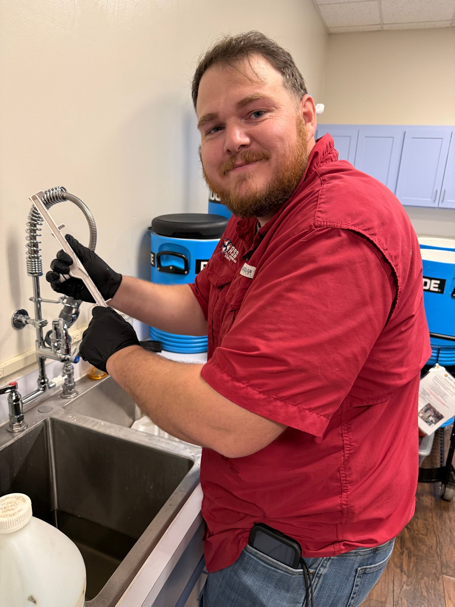 Person in red shirt washing items in a stainless-steel sink with a spray faucet