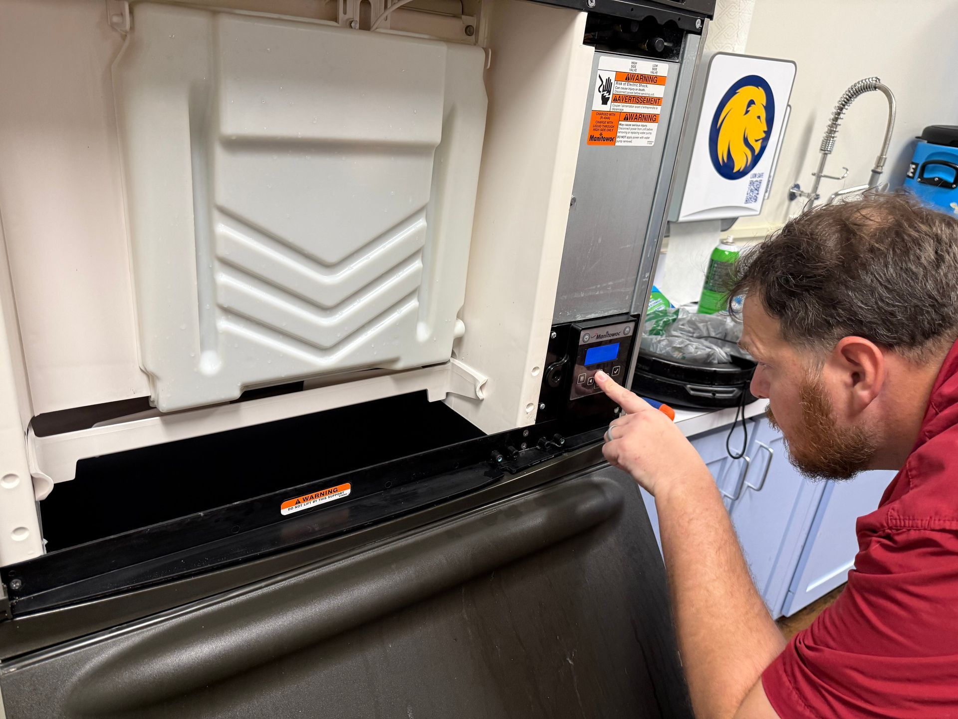 Technician in red shirt inspecting machinery inside an open industrial cabinet