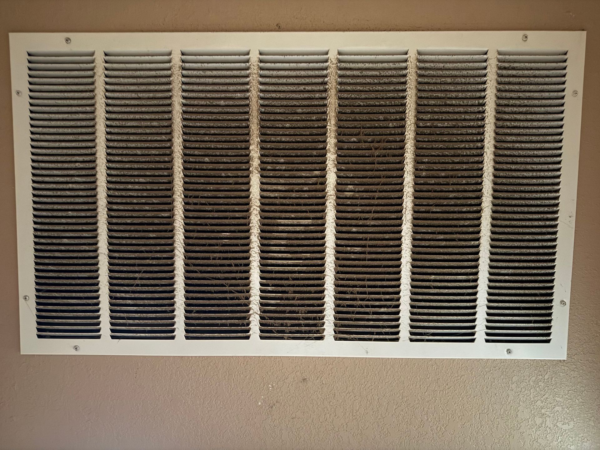 Beige wall vent with horizontal dark slats and visible dust buildup