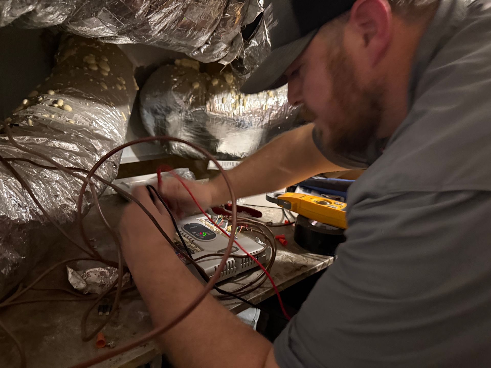 Technician working inside a duct, wiring an electrical panel in an attic with insulated walls.