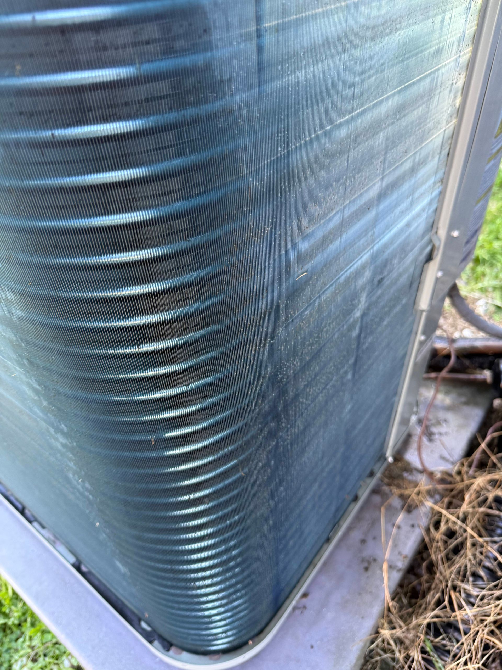 Close-up of a blue metal HVAC condenser coil with bent fins on a concrete base outdoors